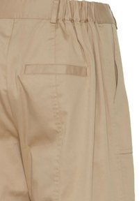 Pantaloni beige con cinturino elastico, tasche laterali e una tasca a pattina sul retro. Texture liscia con vestibilità rilassata.