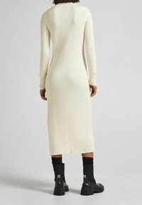 Ribbade, långärmade, krämfärgade stickade klänning med V-formad rygg och en figurnära siluett, i kombination med svarta ankelstövlar.
