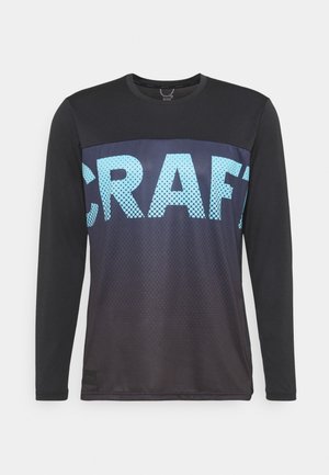 Chemise noire à manches longues avec panneau poitrine bleu foncé et grandes lettres perforées bleu clair formant le mot « CRAFT » sur le devant.