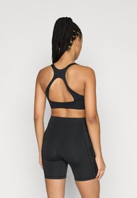 Zwarte sportbeha met een racerback-ontwerp en een uitsnijdingsdetail. Gecombineerd met zwarte, hooggesneden fietsbroekjes, beide gemaakt van rekbaar materiaal.