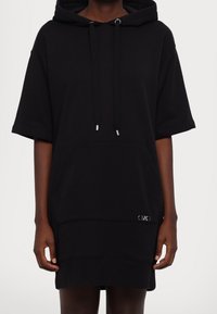 Czarna sukienka dresowa z kapturem wykonana z miękkiego materiału, z krótkimi rękawami, przednią kieszenią i srebrnymi ozdobami. Gładka faktura, minimalistyczny design.