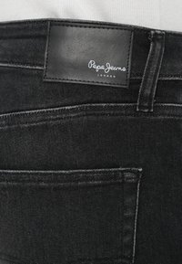 Μαύρο τζιν από τζιν ύφασμα με δερμάτινη ετικέτα στη μέση, διαθέτει ραφές και σχέδιο πίσω τσέπης.