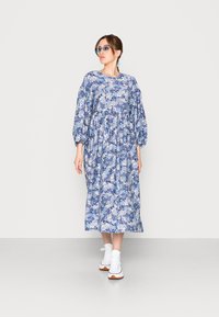 Vestido floral em tons de azul com mangas bufantes, decote redondo e silhueta fluida. Combinado com ténis brancos.