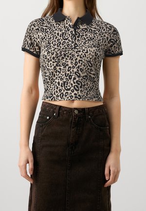 Beskåret polo shirt i beige med sort leopardprint, sort krave og diskrete logo detaljer, parret med en mørk denim nederdel.