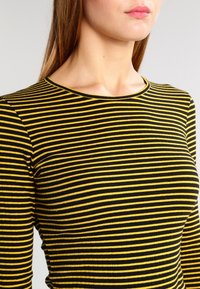 Svart och gulrandig långärmad topp med rund halsringning, som har en ribbad textur och en figurnära design.