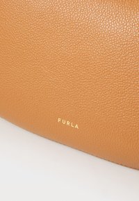 Smeđa torba od teksturirane kože s zlatnim logotipom "FURLA". Površina ima izgled šljunčanog završetka, što ukazuje na trajnost i kvalitetu.