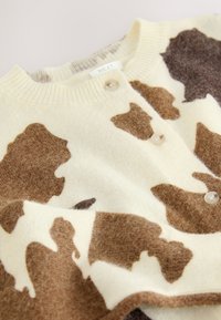 Cardigan en mélange de laine avec une base crème ornée d'un imprimé vache marron, col côtelé, et deux boutons en perle à l'avant.