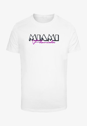 T-shirt en coton blanc avec 'MIAMI' en lettres noires en gras et 'Florida' en cursive rose, agrémenté d'un accent géométrique dans le design.