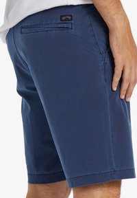 Herren-Shorts in Marineblau, aus glattem Material gefertigt, mit einer Gesäßtasche mit Logopatch, tailliertem Saum und entspanntem Schnitt.