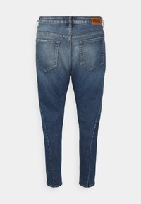 Mörkblå denim jeans med slim fit, utrustade med en brun läderlogg i midjan och två bakfickor.