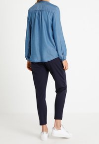 Vaaleansininen farkkutakki pitkät hihat, kerätty selkäosa. Yhdistetty tummien slim-fit-housujen ja metallikoristeisien valkoisten tennareiden kanssa.