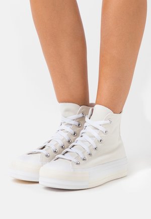 Wysokie trampki z płótna w kolorze off-white z srebrnymi oczkami, białymi sznurówkami, fakturowaną powierzchnią i białą gumową podeszwą.