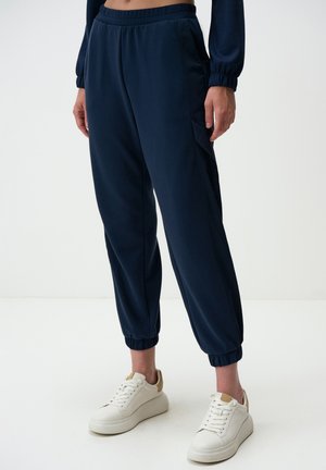 Pantaloni jogger blu navy realizzati in morbido tessuto con cinturino elasticizzato, tasche laterali e polsini aderenti. Abbinati a sneakers bianche con plateau.
