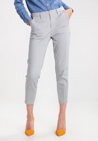 Pantaloni grigi a sigaretta con una texture liscia, tasche frontali e un design aderente. Indossati con tacchi alti gialli brillanti.