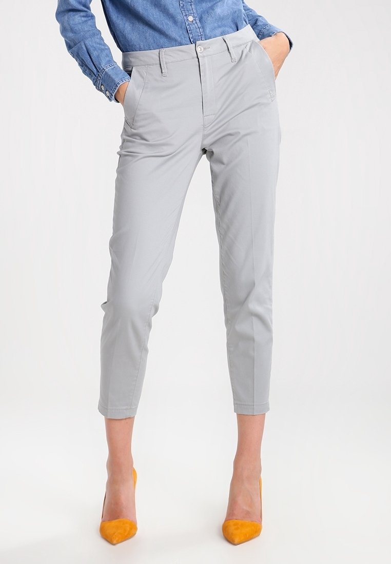 Pantaloni grigi a sigaretta con una texture liscia, tasche frontali e un design aderente. Indossati con tacchi alti gialli brillanti.