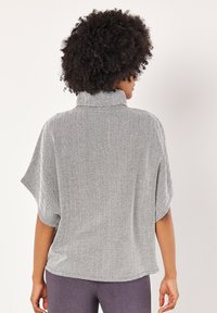 Harmaa ja valkoinen houndstooth-kuvioinen paita, jossa on korkea kaulus, lyhyet hihat ja rento mitoitus. Pehmeä rakenne, kevyt kangas.