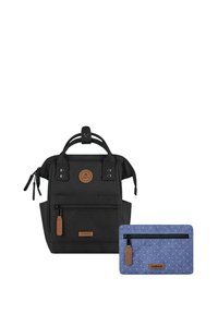 Schwarzer Rucksack aus strukturiertem Stoff mit zwei seitlichen Reißverschlüssen, einem Griff und einem braunen Logopatch. Enthält ein kleines blaues Täschchen mit weißen Punkten.