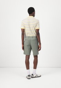 Grønne shorts med en glat tekstur og baglommer, parret med en stribet gul og lys lilla kortærmet polo skjorte.