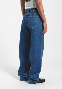 Jeans de pierna ancha en azul, hechos de mezclilla. Cuentan con cinco bolsillos, costuras visibles y una cintura alta, con una etiqueta en la parte trasera.