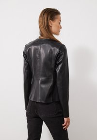 Giubbotto in pelle nera con design aderente, texture liscia e colletto arrotondato. La parte posteriore presenta dettagli a pannello e spalle senza cuciture.