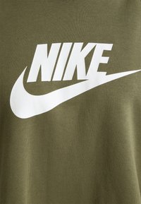 Oliivinvihreä puuvillainen t-paita, jossa on iso valkoinen "NIKE" -logo ja swoosh-grafiikka. Kangas on sileä ja rento malli.