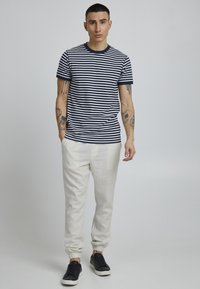 Camiseta de algodón a rayas en azul marino y blanco con cuello redondo; combinada con pantalones jogger de color claro y zapatillas negras. Mangas cortas, corte casual.