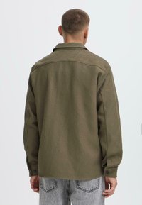Olive green corduroy shirt with a collar, long sleeves, and button cuffs. Features a textured fabric and relaxed fit.