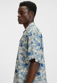 Lyhythihainen paita vaaleansinisellä sävyllä, jossa on tummansinisellä ja valkoisella kukkakuosi. Paidassa on kaulus ja rento malli pehmeästä kankaasta.