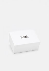 Biały prostokątny pojemnik o gładkiej fakturze, z logo "KARL LAGERFELD" w kolorze czarnym na górze. Projekt jest minimalistyczny i elegancki.