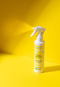 Bottiglia di spray condizionante bifasico bianca e gialla che spruzza una nebbia su uno sfondo giallo brillante.