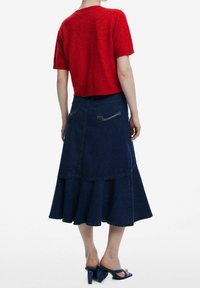 Punainen lyhythihainen neulepaita, joka on yhdistetty tummansinisestä farkkukankaasta valmistettuun leveälahkeiseen hameeseen, jossa on liikkuva helma ja kaksi takataskua. Asusteena siniset korolliset sandaalit.