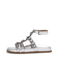 Sandal in argento metallico con più cinturini, abbellita con strass e una fibbia, caratterizzata da una suola piatta e una suola esterna color beige testurizzato.