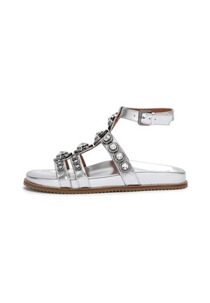 Silver metallic sandal with multiple straps, embellished with rhinestones and a buckle, featuring a flat sole and textured tan outsole.