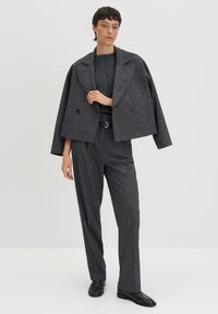 Veste cropped grise texturée avec grands revers, assortie à un haut à manches longues et un pantalon large élégant. Des chaussures noires viennent compléter le look.