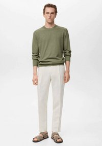 Green knit sweater, cream tapered trousers, and brown sandals. Simple design with soft texture and neutral color palette.