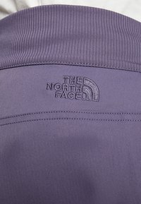 Fialová tkanina s texturovaným vzorem, s výrazným herringbone vzorem. Logo The North Face je vyšívané ve světlejším odstínu.