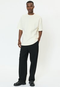 Fehér, túlméretezett póló kerek nyakkivágással és rövid ujjakkal, laza fekete nadrággal és fekete fűzős cipővel párosítva.