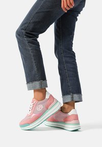 Sneakers rosa e bianchi realizzati in mesh e camoscio, con una suola spessa e dettagli verdi, e un logo sul lato. Jeans con risvolti.