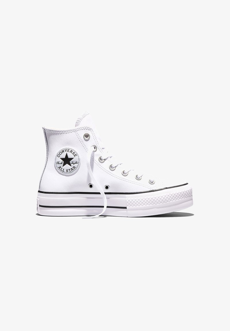Baskets montantes blanches Converse All Star avec une bande noire sur la semelle et un patch rond visible avec le logo sur le côté.