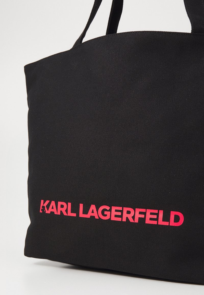 Sac fourre-tout noir en tissu texturé, arborant une marque « KARL LAGERFELD » rose vif d'un côté et de solides anses doubles.