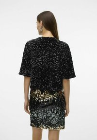 Top negro con lentejuelas y mangas cortas, combinado con una falda brillante que transiciona de lentejuelas negras a doradas, con una textura suave en todo.