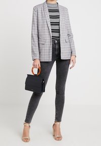 Šedý kostkovaný blazer s klopem, černobílý pruhovaný top, tmavé skinny džíny a černá kabelka s oranžovými rukojeťmi. Zlacené sandály na podpatku.