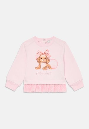 Sudadera rosa con un gráfico de un cachorro con un lazo, decorada con texto brillante. En la parte inferior tiene una capa con volantes y lunares.