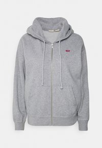 Sudadera gris con cremallera hecha de una mezcla de algodón, con capucha ajustable, bolsillos frontales y un pequeño logo rojo en el lado izquierdo del pecho.