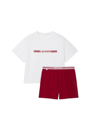 Camiseta blanca de algodón con el texto rojo "LACOSTE" y acentos a rayas, combinada con pantalones cortos rojos con cintura elástica y logo de la marca.