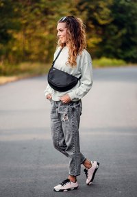 Černá crossbody taška, svetle zelená mikina, potrhané šedé džíny a růžové tenisky s černými akcenty. Kučeravé vlasy upravené ležérně.