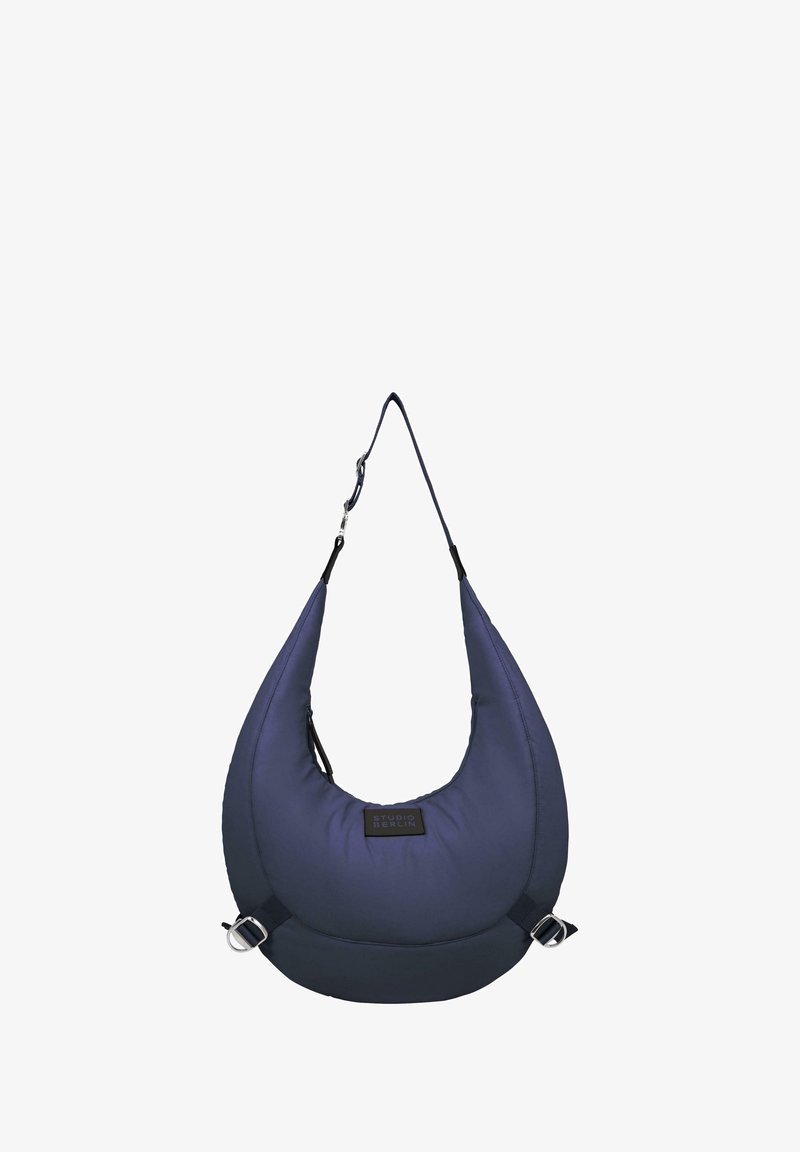 Borsa a spalla imbottita blu Navy con design curvo, tracolla regolabile e finiture in metallo argentato. Presenta un'etichetta del marchio sul davanti.