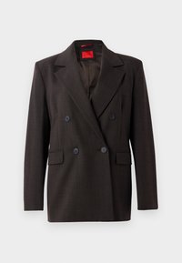 Blazer de color marrón oscuro de doble botonadura con solapas pico, dos bolsillos frontales y botones negros. Textura suave y ajuste entallado. Etiqueta interior roja.