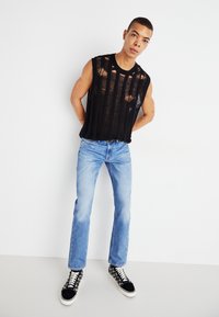 Top nero senza maniche, a costine con righe verticali, abbinato a jeans in denim blu chiaro e sneakers nere e bianche con motivo.