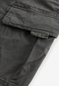 Dunkelgrauer Stoff mit glatter Textur; verfügt über eine Klapptasche und einen seitlichen Riegel. Die Nähte sind entlang der Kanten sichtbar.